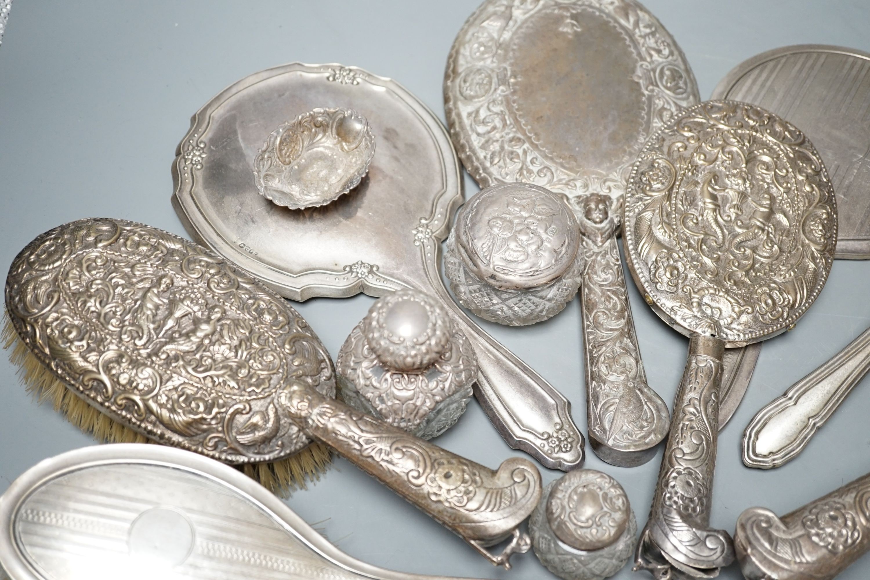 A mixed collection of four silver mounted vanity mirrors, four assorted clothes brushes, (including set of three), three silver mounted glass jars and a small silver dish.